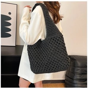 Detail of black crochet tote bag with woven texture worn over a white suit jacket