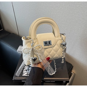 Detail of beige quilted handbag featuring pearl bow, heart charm, and lace ribbon decoration