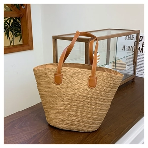 Detailed close-up of handmade straw tote bag with brown leather handles on wooden table