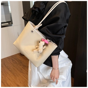 Detail of off-white lychee texture tote bag with plush puppy pendant and knotted shoulder strap