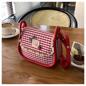 Detail of red gingham canvas crossbody bag with lace trim and strawberry pendant on a table