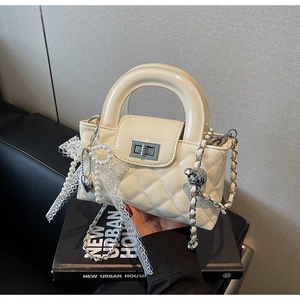 Detail of quilted beige patent leather mini bag with lace bow and pearl heart charm