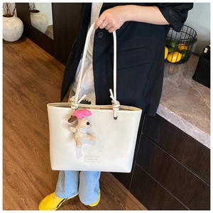 Close-up of white lychee grain crossbody bag with cute plush puppy charm and brand label