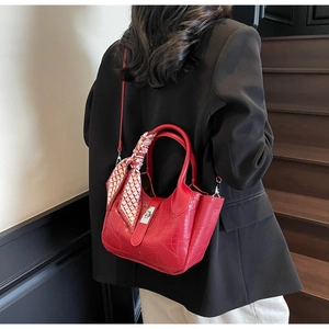 Detail of red croc-effect bucket bag with silk scarf on handle and silver twist lock