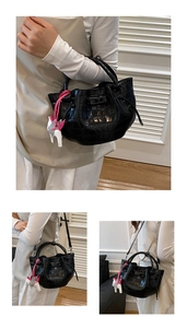 Detail of black crocodile texture bucket bag with horse charm and detachable strap