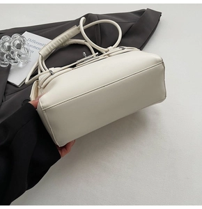 Detailed close-up of cream-white leather trapezoid bag with silver buckle and round handle