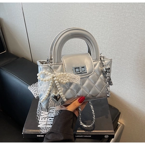 Detail of silver quilted handbag with metal clasp, pearl bow charm, and chain strap