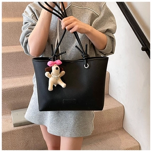 Close-up of black lychee grain leather tote bag worn by model with cute dog charm