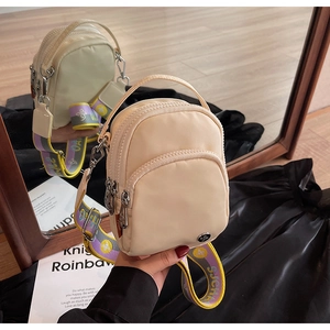 Détail d'un mini sac beige en nylon avec une large bandoulière colorée vue dans un miroir
