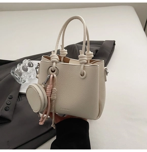 Close-up of beige lychee leather bucket bag with knot handle and tassel charm