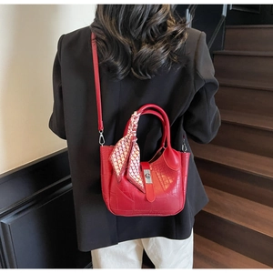 Detail of red crocodile embossed bucket bag with a silk scarf tied on the handle