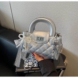 Detailed macro of silver quilted handbag featuring a pearl lace bow and metal rotary lock