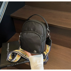 Détail du sac bandoulière en nylon noir avec sangle jacquard et trois poches zippées