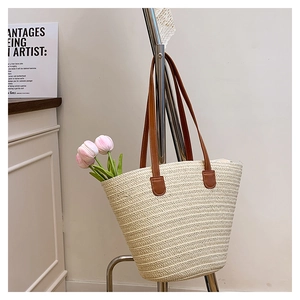 Detail of cream woven tote bag featuring brown leather straps on a minimalist stand