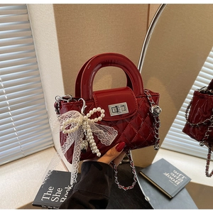 Detail of red quilted patent leather bag featuring pearl bow and silver twist lock