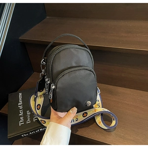 Détail de sac bandoulière en nylon noir avec sangle florale sur un escalier