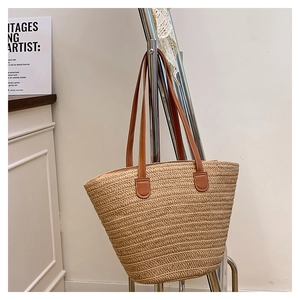 Detail of hand-woven straw tote bag with brown leather handles on a minimal hanger