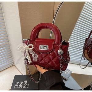 Detail of burgundy quilted patent leather handbag with pearl bow charm and metal clasp
