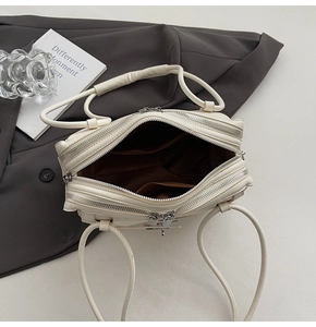 Top view of cream-colored shoulder bag showing multiple zipper compartments and brown lining