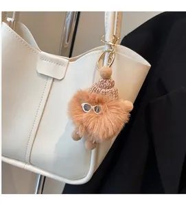 Brown plush monster bag charm with glasses and knit hat on a white tote bag