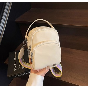 Vue détaillée du mini sac bandoulière en nylon crème avec sangle colorée sur bois