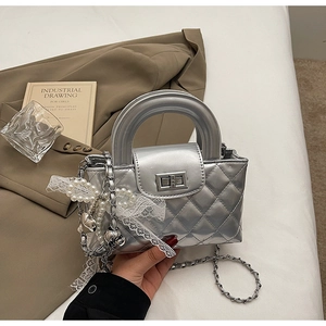 Detail of silver quilted bag with lace trim, pearl charms, and metallic chain strap