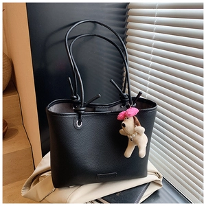 Detail of black pebbled leather tote bag with knotted straps and cute dog charm accent
