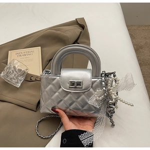 Detailed close-up of a silver quilted handbag with pearl charms and lace decoration
