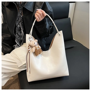 Detail of white leather tote bag with a cute brown teddy bear charm on the strap
