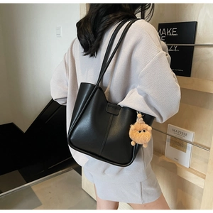 Detail of black leather bucket bag with plush lion charm and adjustable buckle strap
