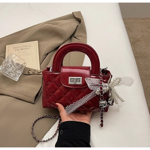 Detail of red quilted patent leather bag with silver lock and pearl lace bow charm