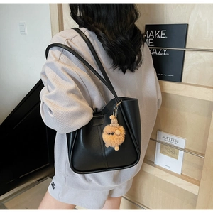 Close-up of black synthetic leather tote bag with a creative plush pompom charm and straps