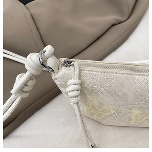 Details von Blumenstickerei und Knotengurt an eleganter cremefarbener Handtasche