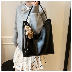 Detail of black faux leather tote with textured finish and a cute plush bear charm