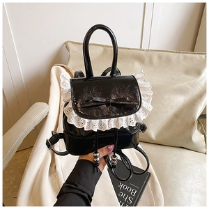 Detail of black patent leather mini backpack featuring white lace trim and bow accent
