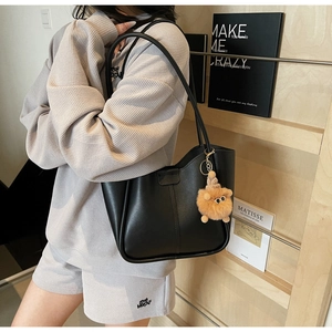 Minimalist black faux leather tote bag with brown plush charm shown on a model
