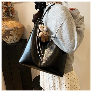 Detailed view of large black glossy tote bag with cute bear charm and premium PU leather texture