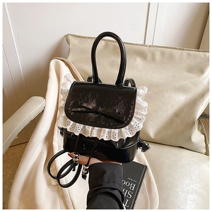 Detail of black patent mini backpack with delicate white lace trim and bow accent