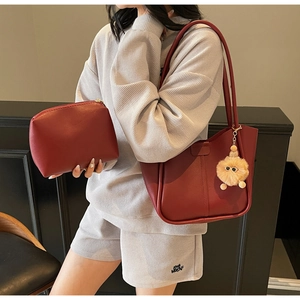 Deep red leather tote and pouch set with plush charm shown in a minimalist setting