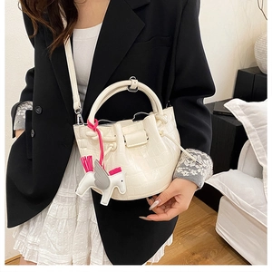 Detailed shot of white crocodile pattern bucket bag with a colorful horse charm on model