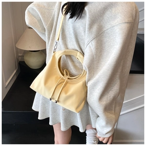 Detail of a creamy yellow bucket bag with round handle and silver metallic drawstring beads