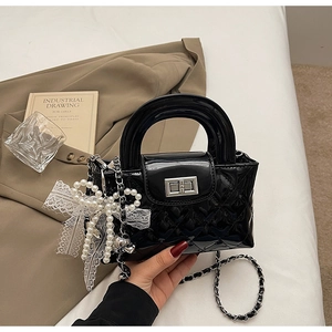 Detail of black patent leather mini bag with quilted pattern and pearl bow charm