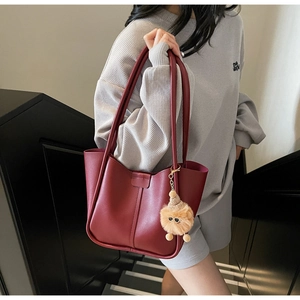Detailed view of the dark red tote bag with dual straps and a plush bear charm on the side