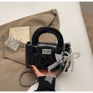Detail of black quilted patent leather bag with lace bow and pearl chain charm