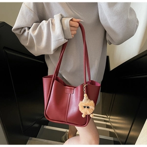Close-up of deep red tote bag with plush charm and detailed stitching on stairs