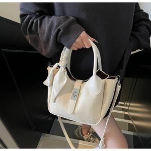 Detail of cream crocodile embossed bucket bag with gold lock and decorative silk scarf