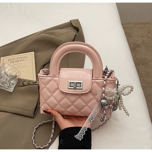 Close-up of pink patent leather crossbody bag with quilted pattern and pearl charm