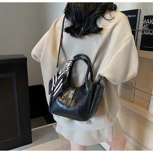 Detail of black crocodile embossed leather bucket bag with silk scarf on model