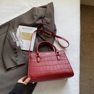 Dettaglio borsa rossa con trama a coccodrillo, manici tondi e piedini di appoggio