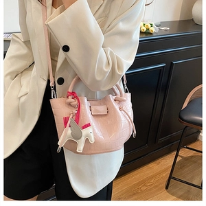 Detail of pink croc-embossed bucket bag with white pegasus charm and drawstring closure